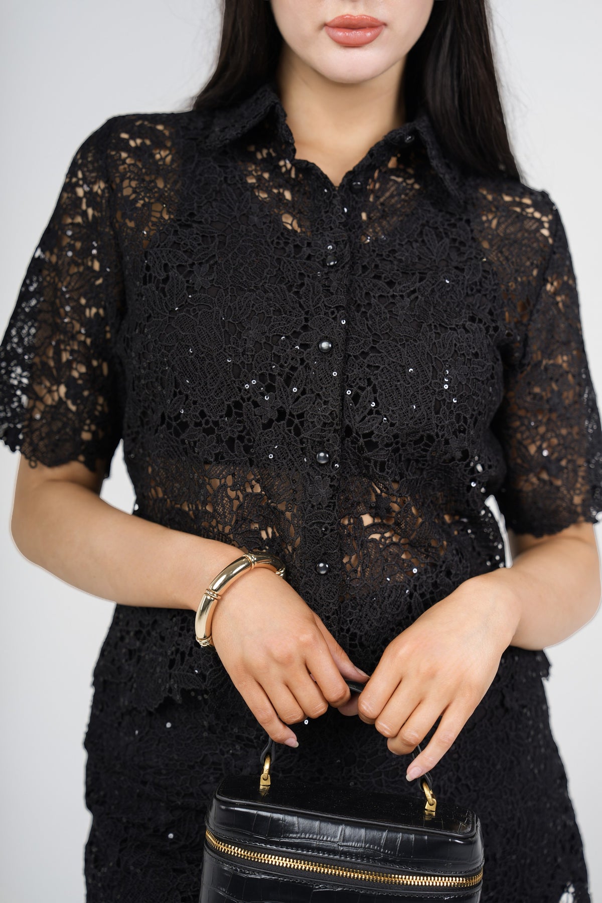 A woman wearing a black lace short-sleeve button-up blouse with sequined details