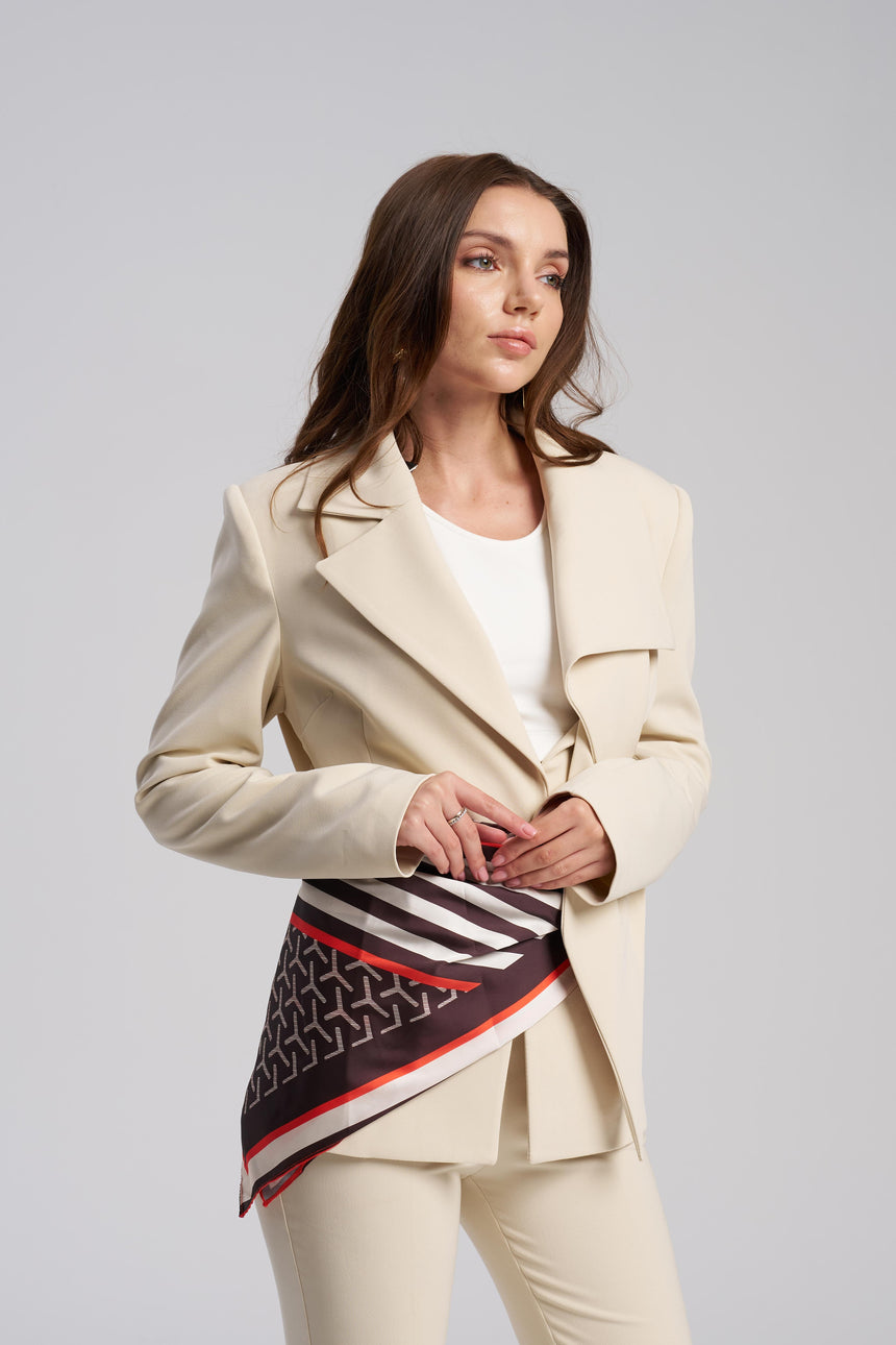 Woman wearing a beige suit with a patterned scarf on a gray background