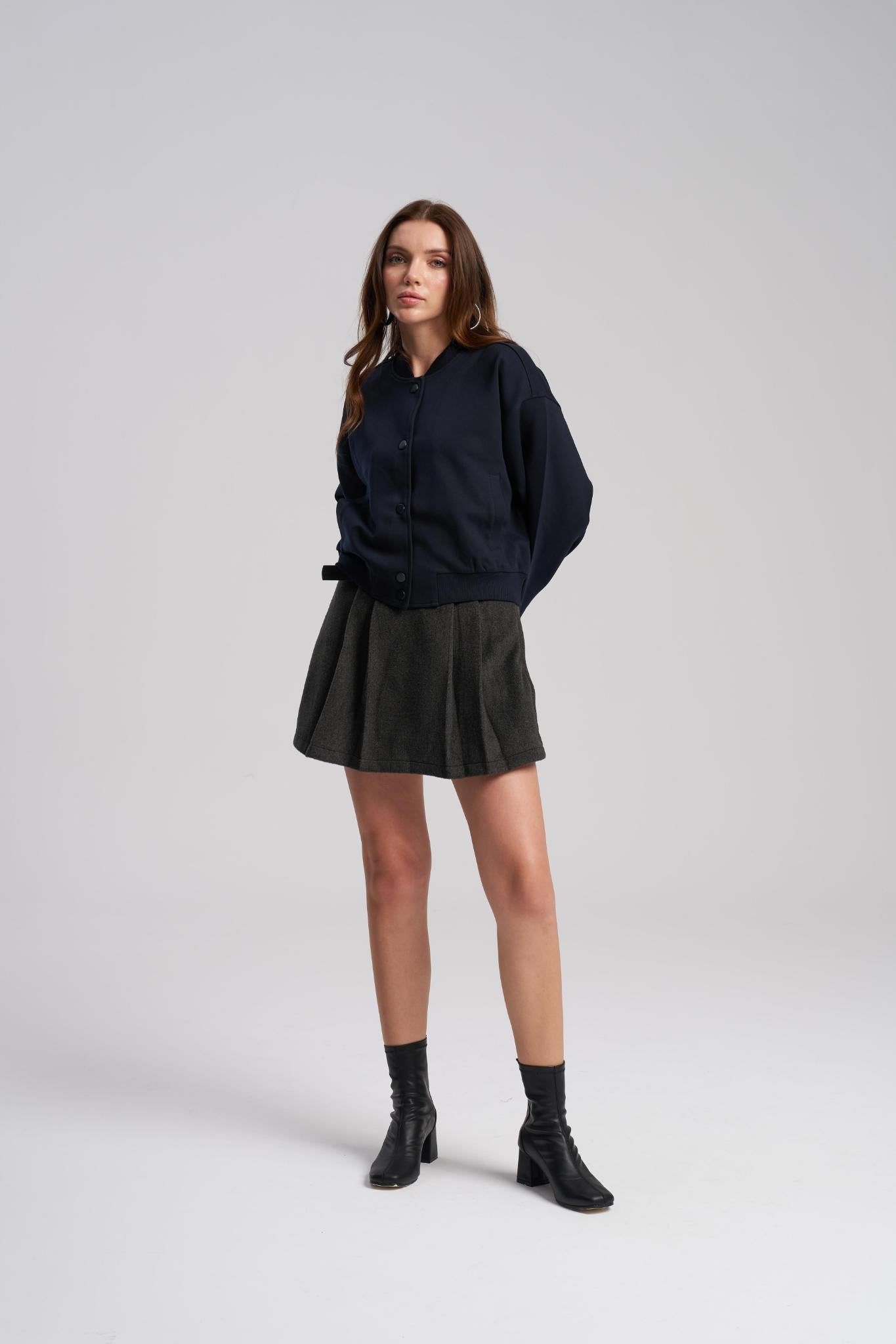 Woman wearing a navy sweater, black skirt, and black boots on a white background