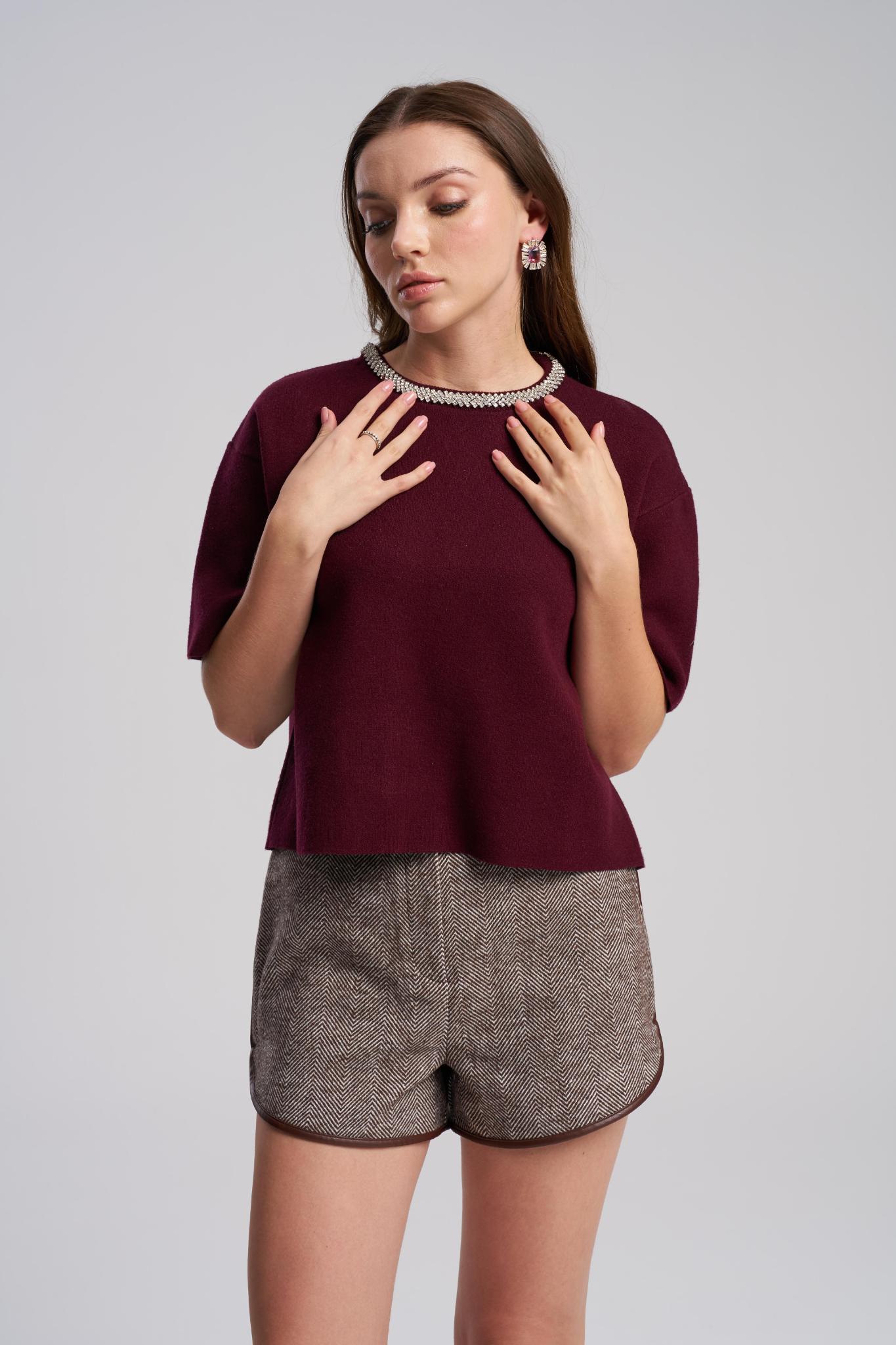Woman wearing a burgundy top with a textured collar and gray shorts on a light gray background