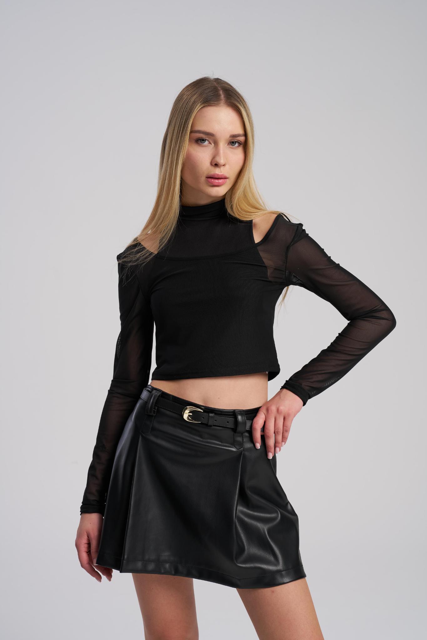 Woman wearing a black long-sleeve top with sheer sleeves and a black skirt on a gray background
