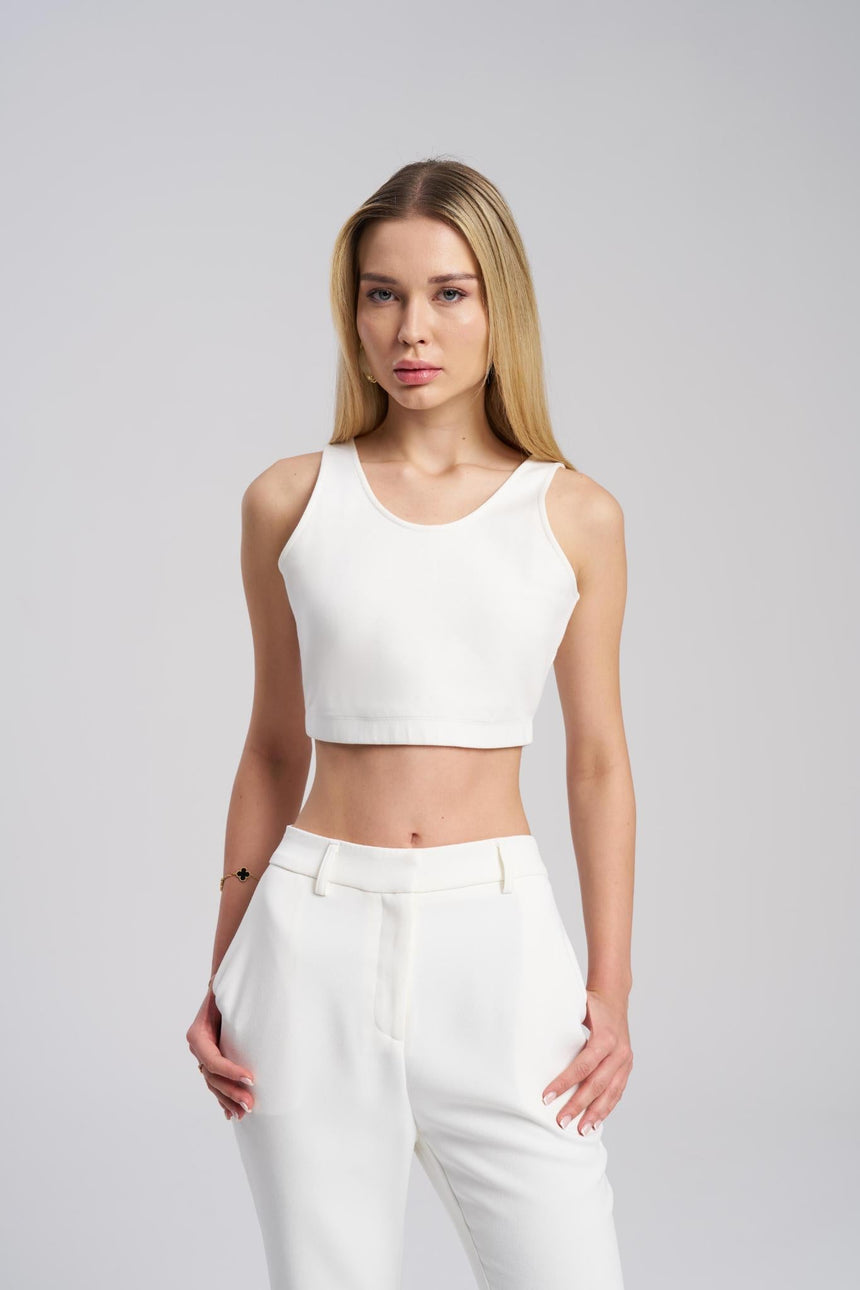 Woman wearing a white sleeveless top and pants on a gray background