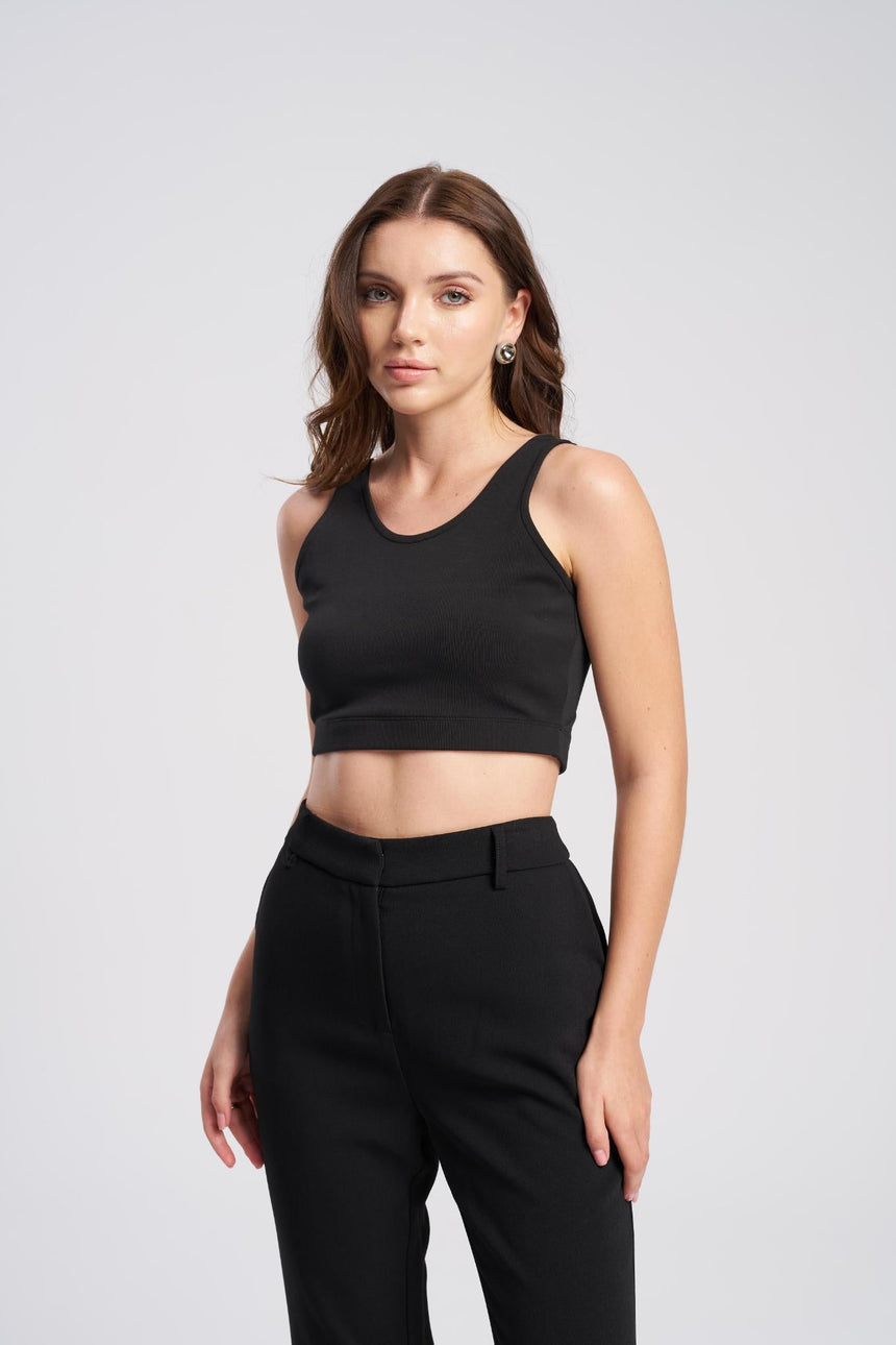 Woman wearing a black sleeveless top and black pants on a light gray background