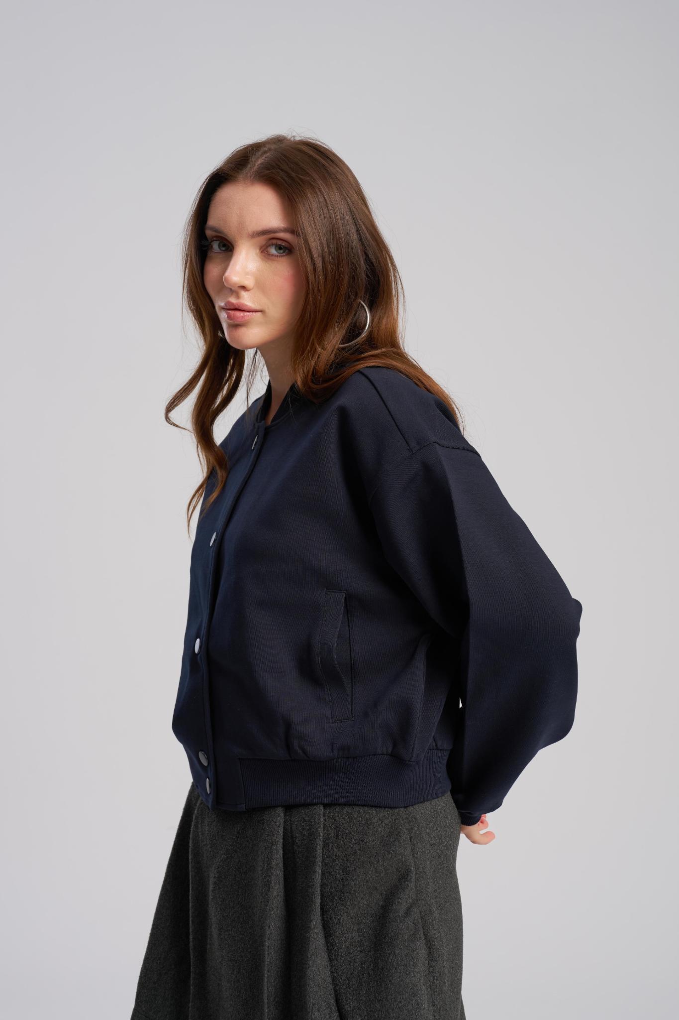 Woman wearing a navy blue bomber jacket on a gray background