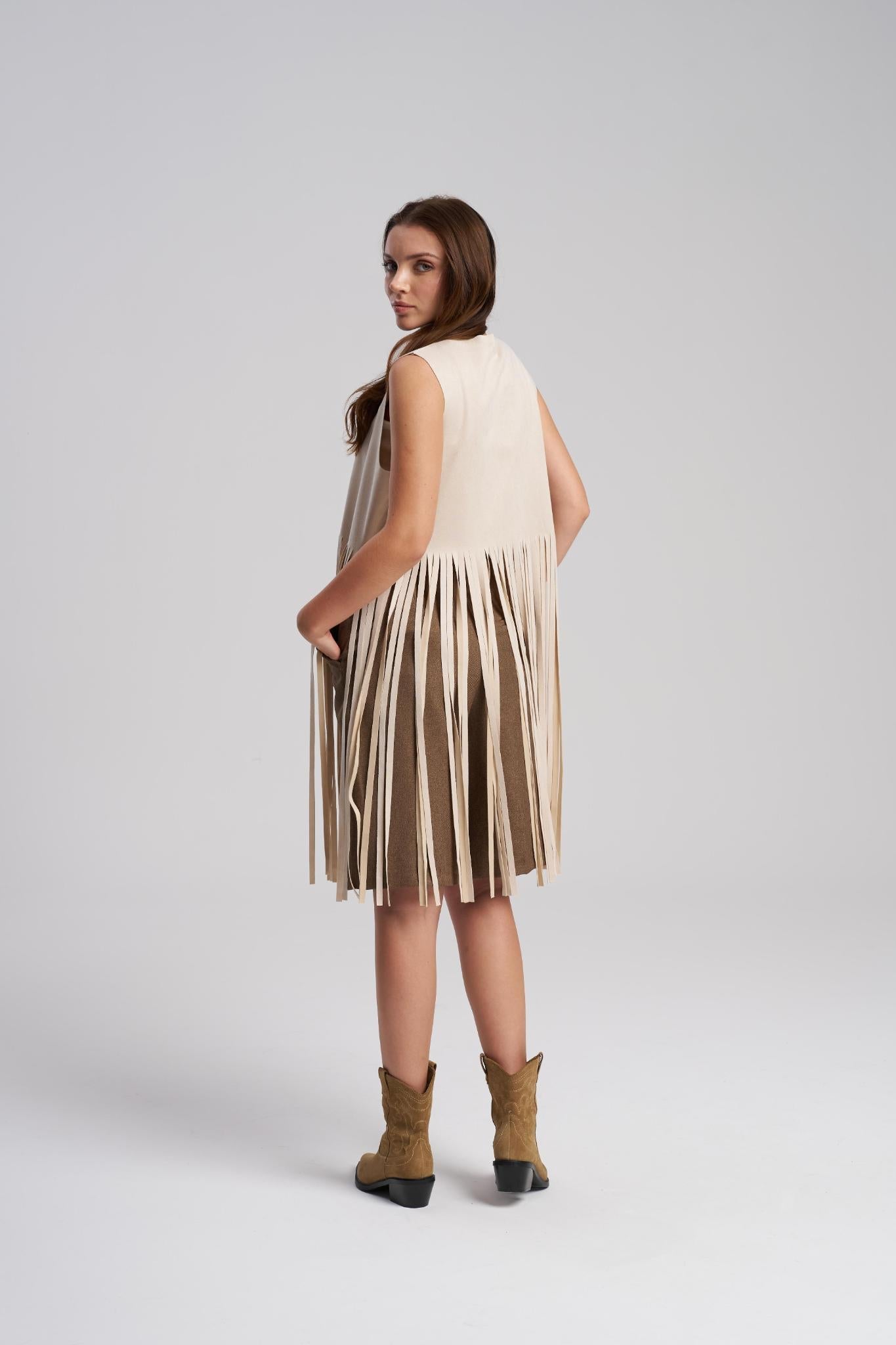 Woman wearing a beige sleeveless vest with fringe details on a white background