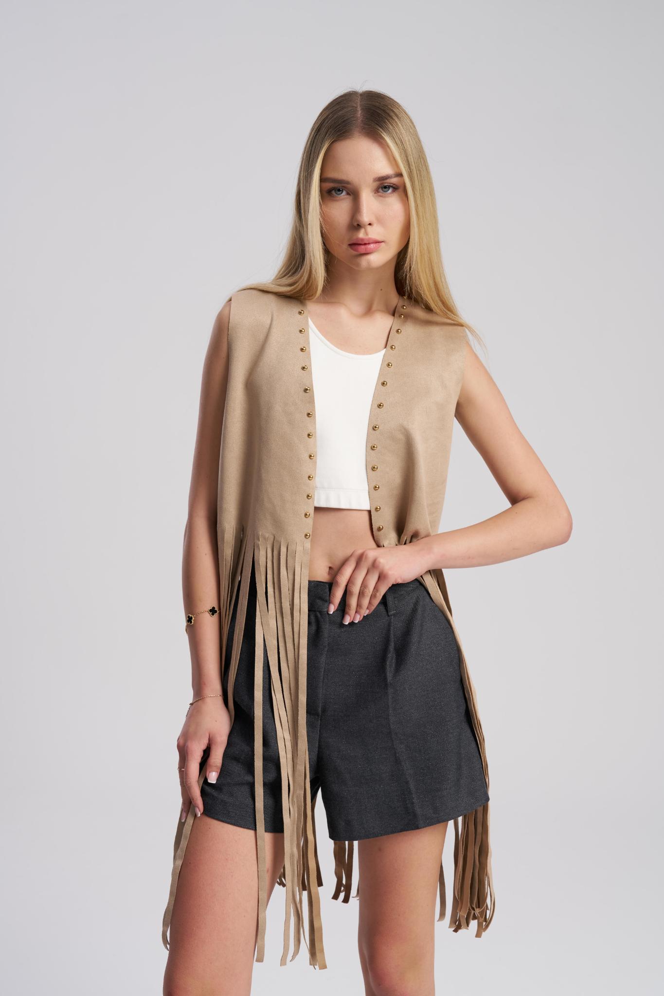 Woman wearing a beige fringe cardigan over a white top and black shorts on a light gray background