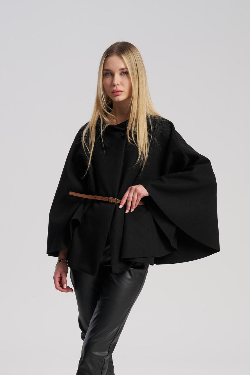 Woman wearing a black poncho over a black outfit on a light gray background