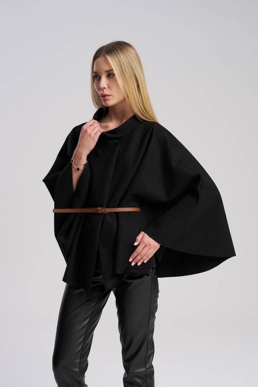 Woman wearing a black poncho with a brown belt on a gray background