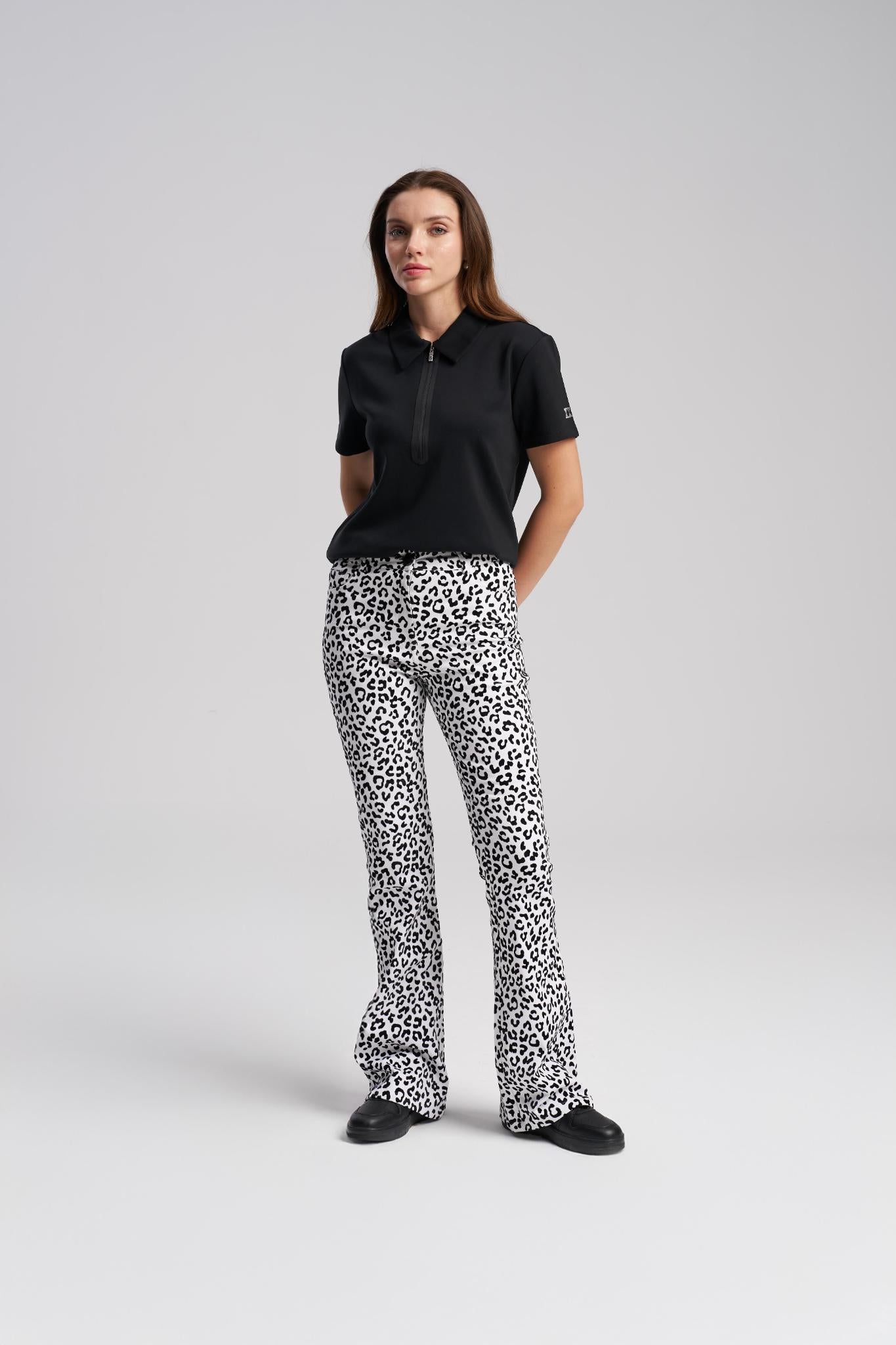 Woman wearing a black polo shirt and leopard print pants on a gray background
