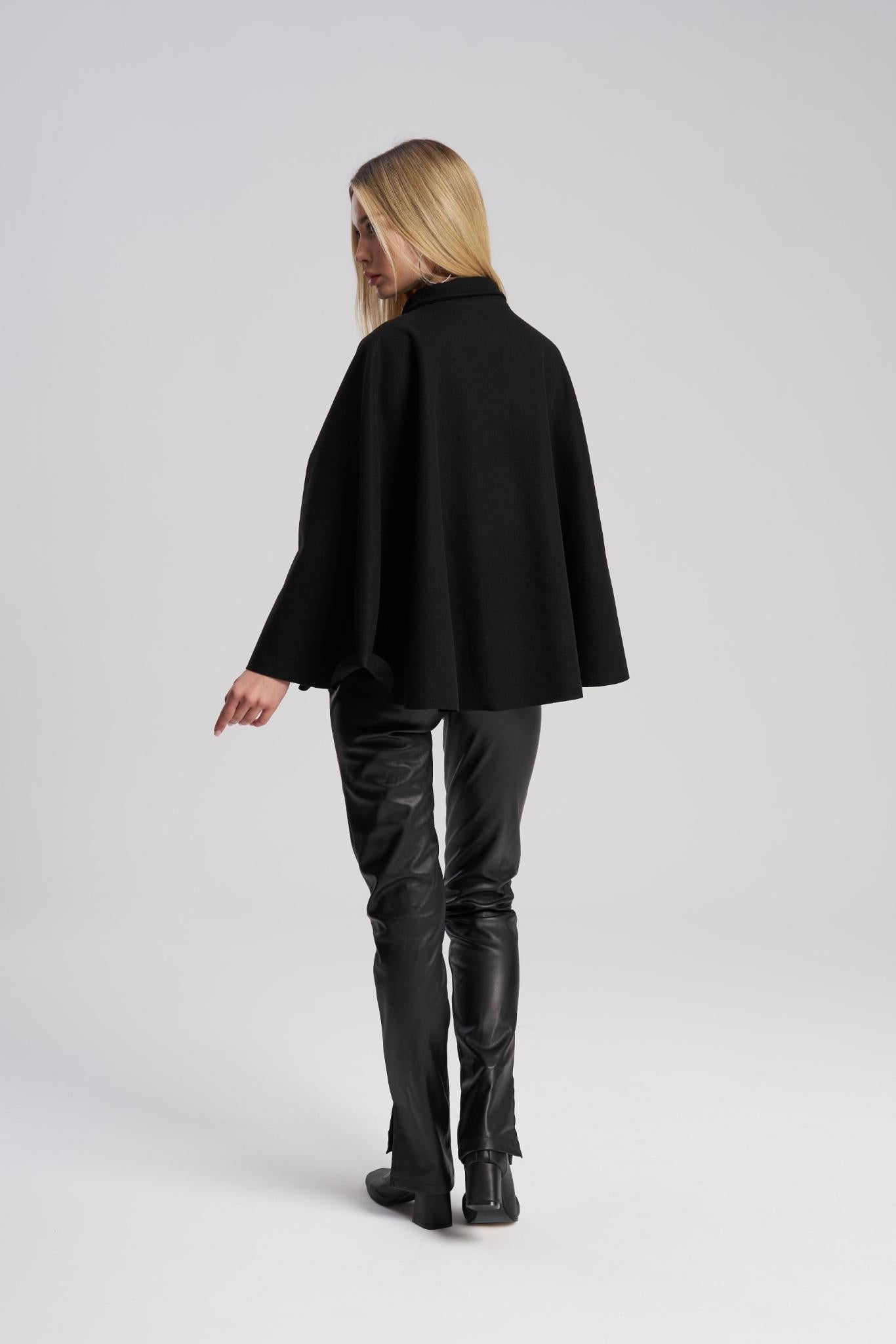 Person wearing a black cape and leather pants on a white background