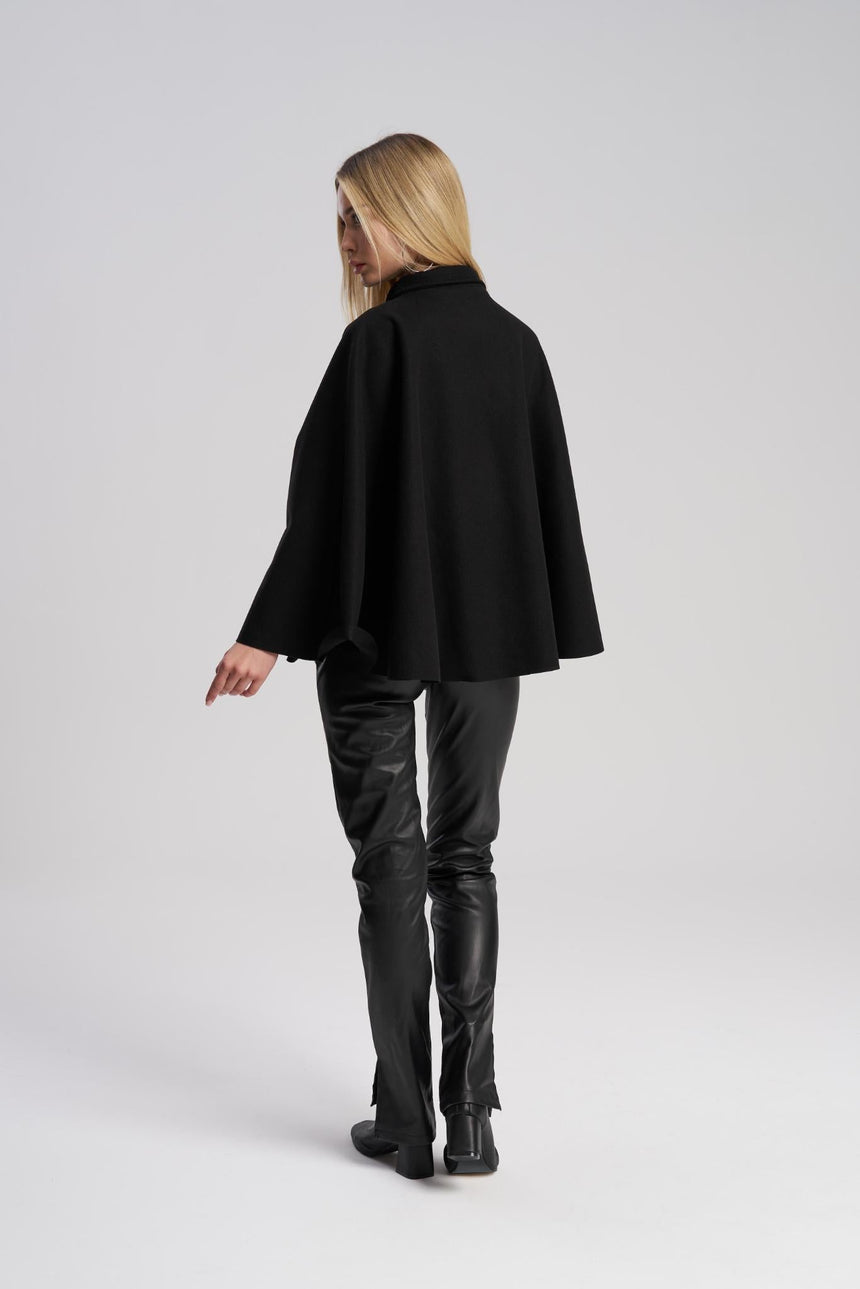 Person wearing a black cape and leather pants on a white background