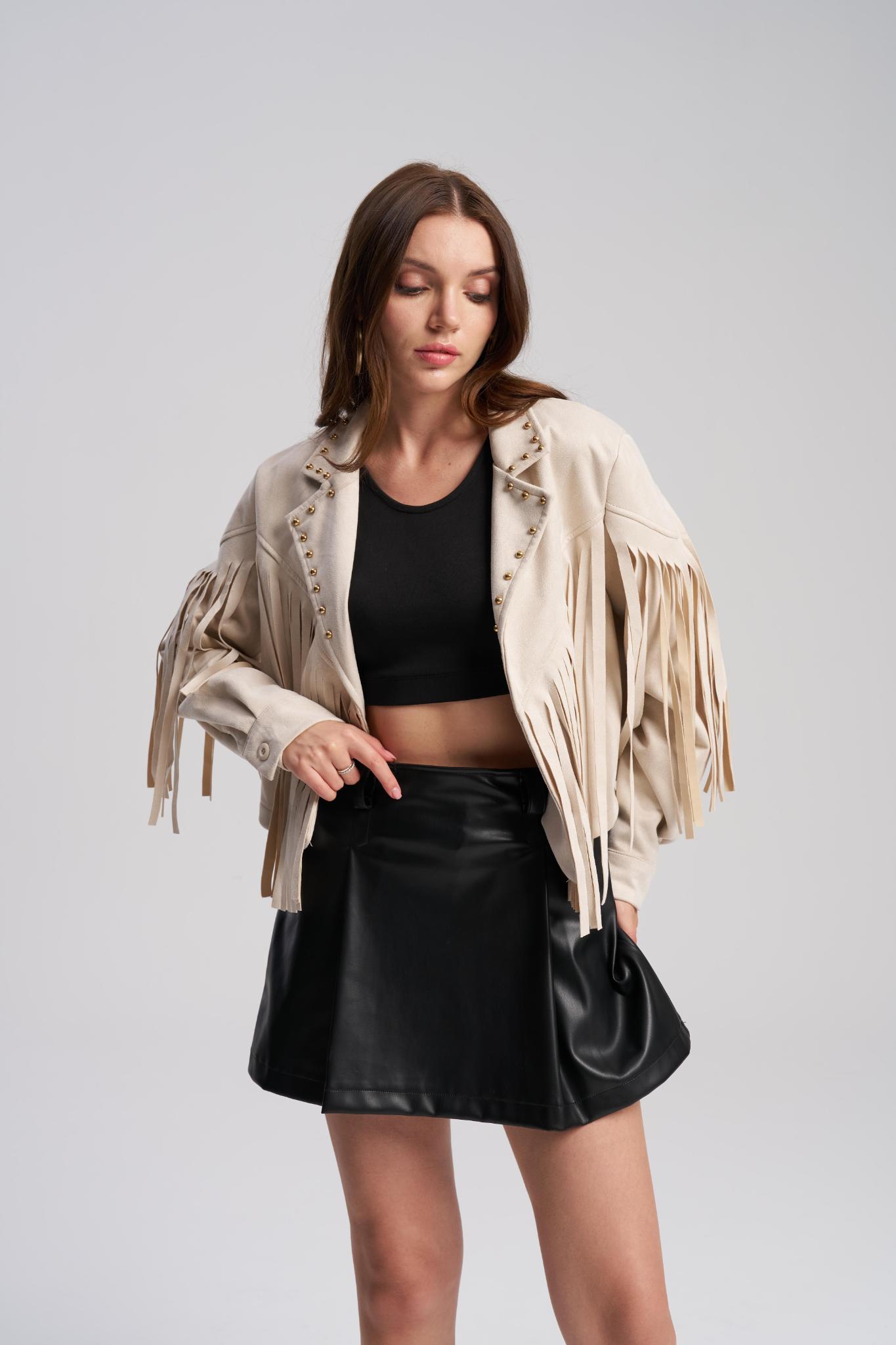 Woman wearing a beige fringe jacket, black top, and leather skirt on a gray background