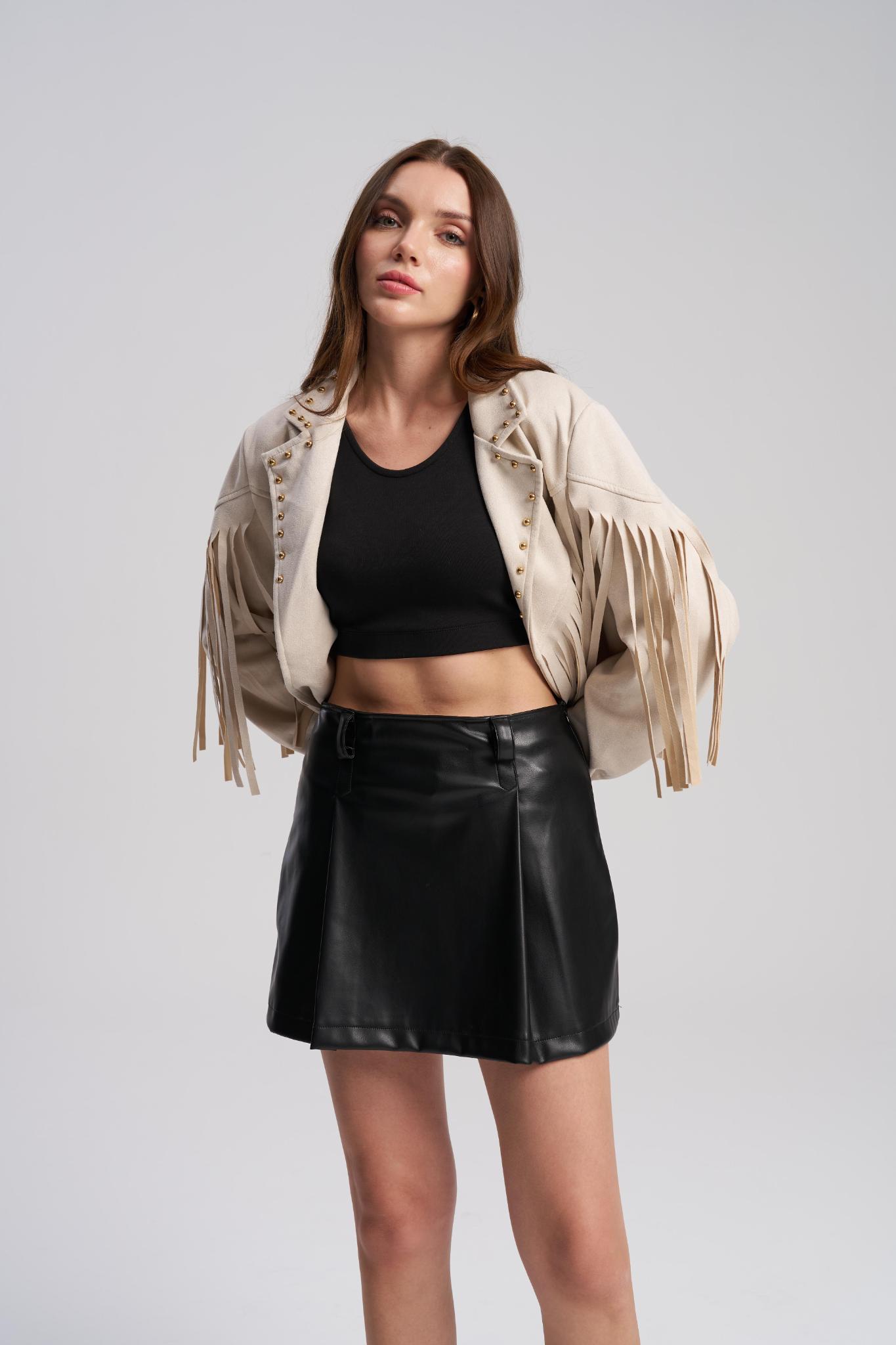 Woman wearing a beige fringed jacket, black top, and black leather skirt on a white background