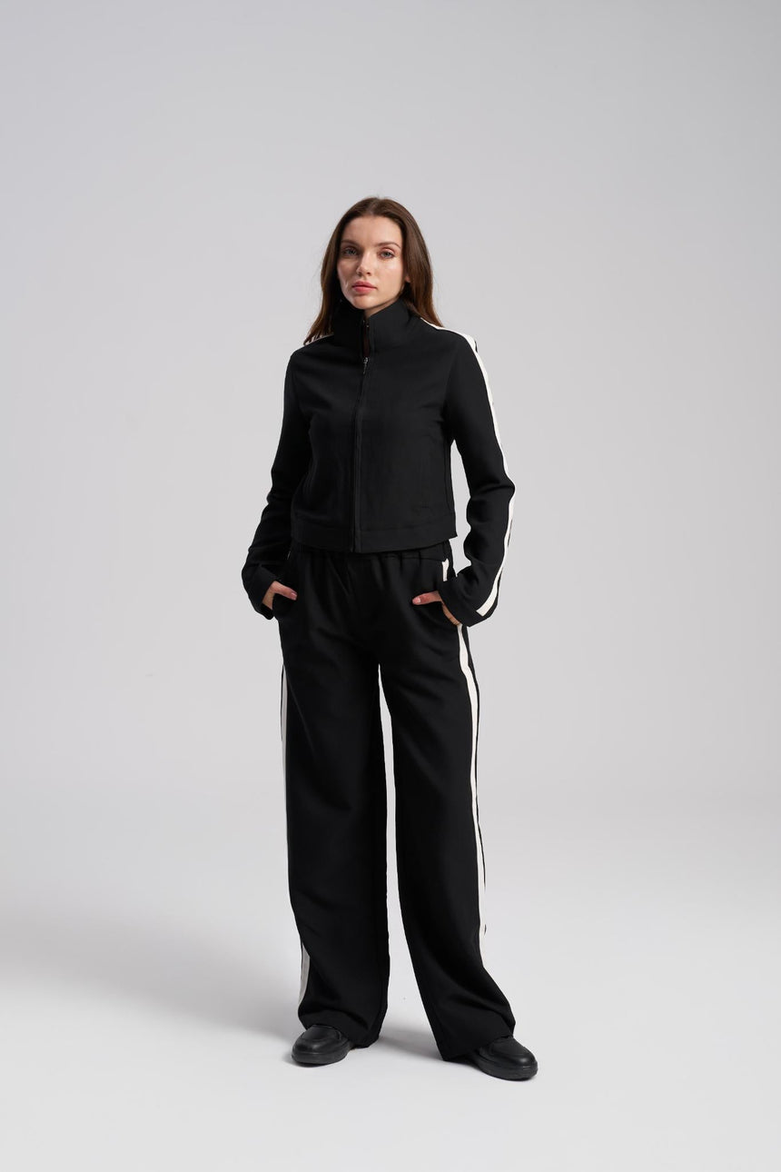 Woman wearing a black tracksuit with white stripes on a gray background