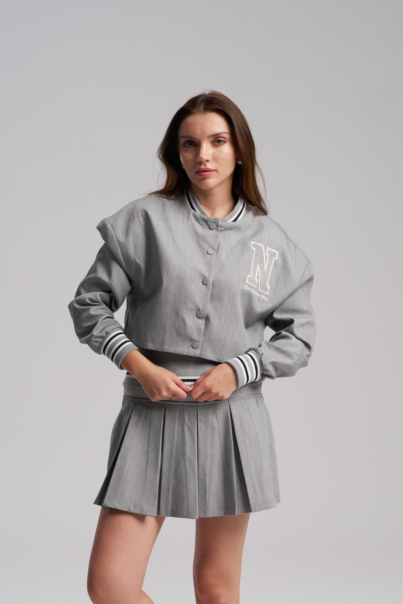 Woman wearing a gray varsity jacket and skirt on a plain background