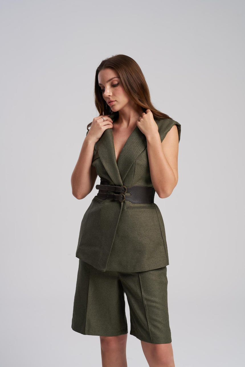 Woman wearing a green suit with a belt on a gray background