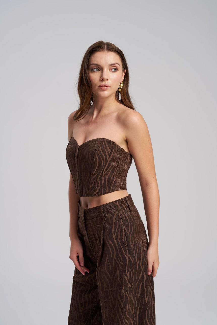 Woman wearing a brown strapless top and wide-leg pants with a subtle pattern on a gray background