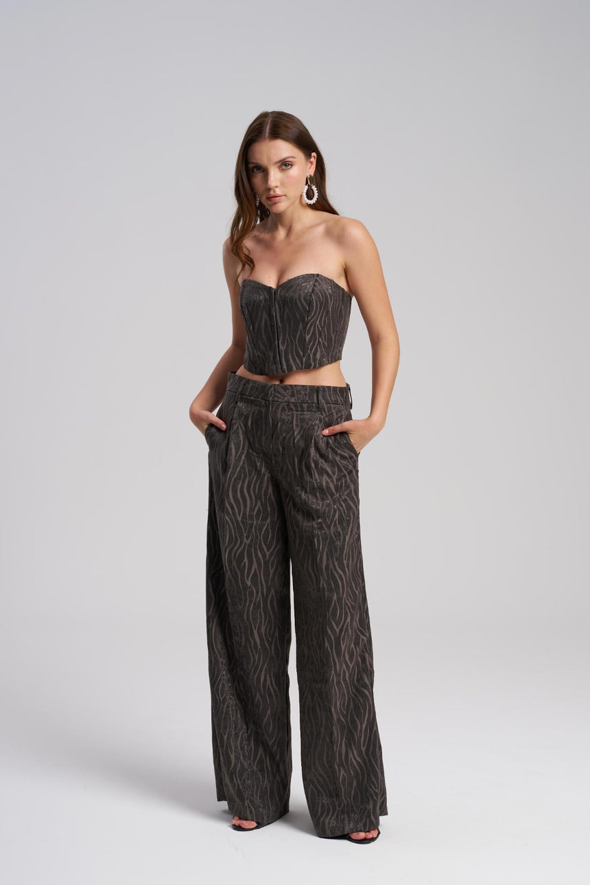 Woman wearing a patterned strapless top and wide-leg pants on a light gray background