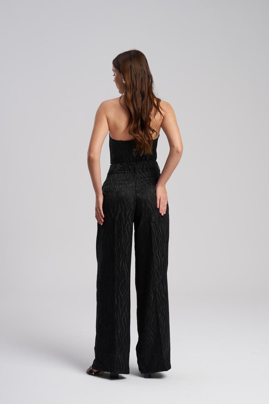 Woman wearing a black strapless top and wide leg pants on a white background