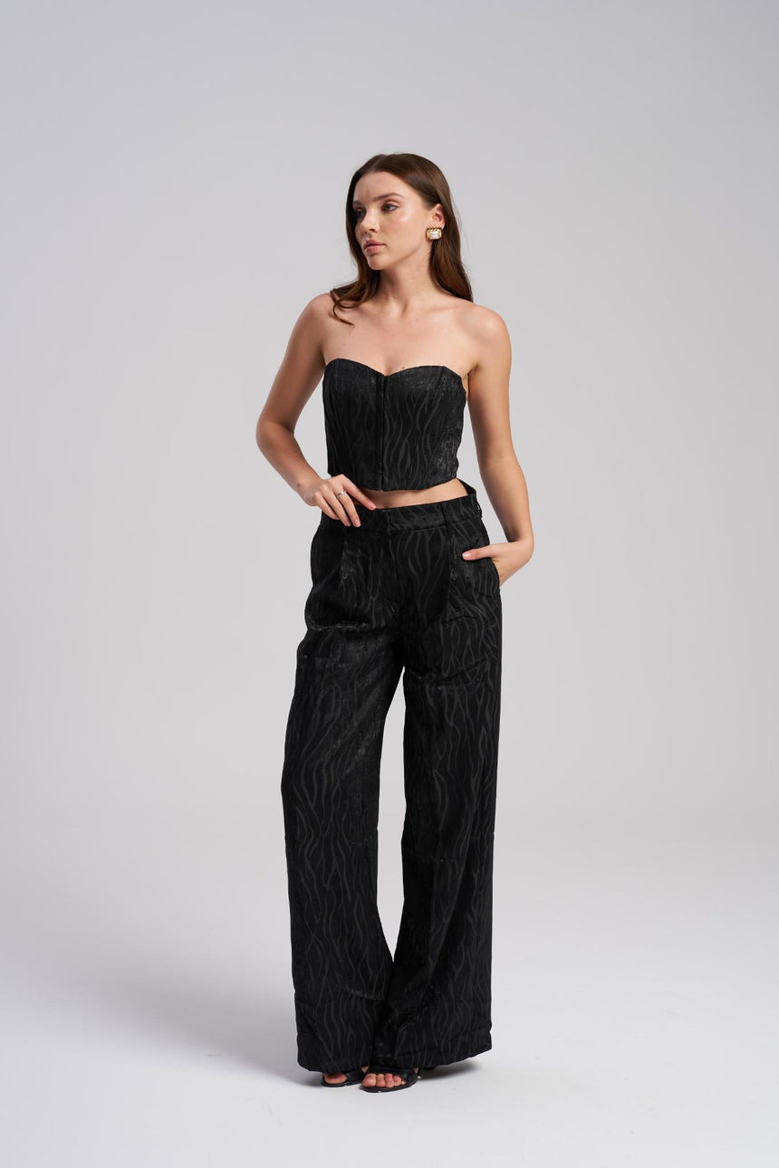 Woman wearing a black strapless top and wide-leg pants on a gray background