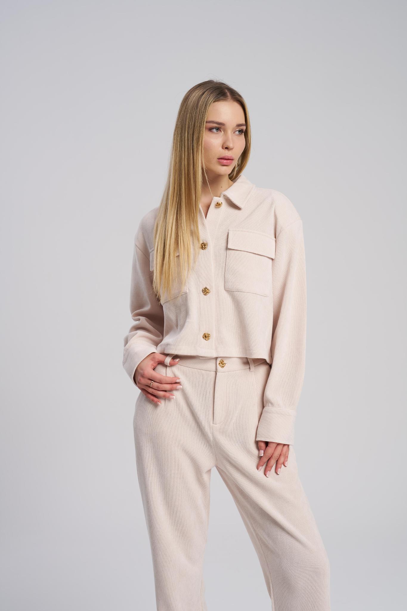Woman wearing a beige outfit with a jacket and pants on a plain background