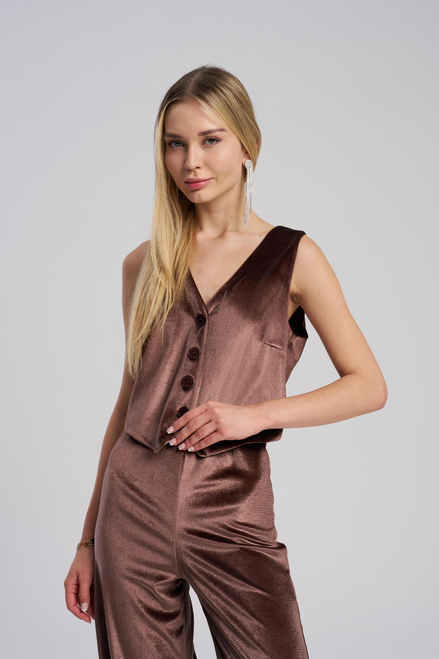 Woman wearing a brown sleeveless top and pants on a plain background