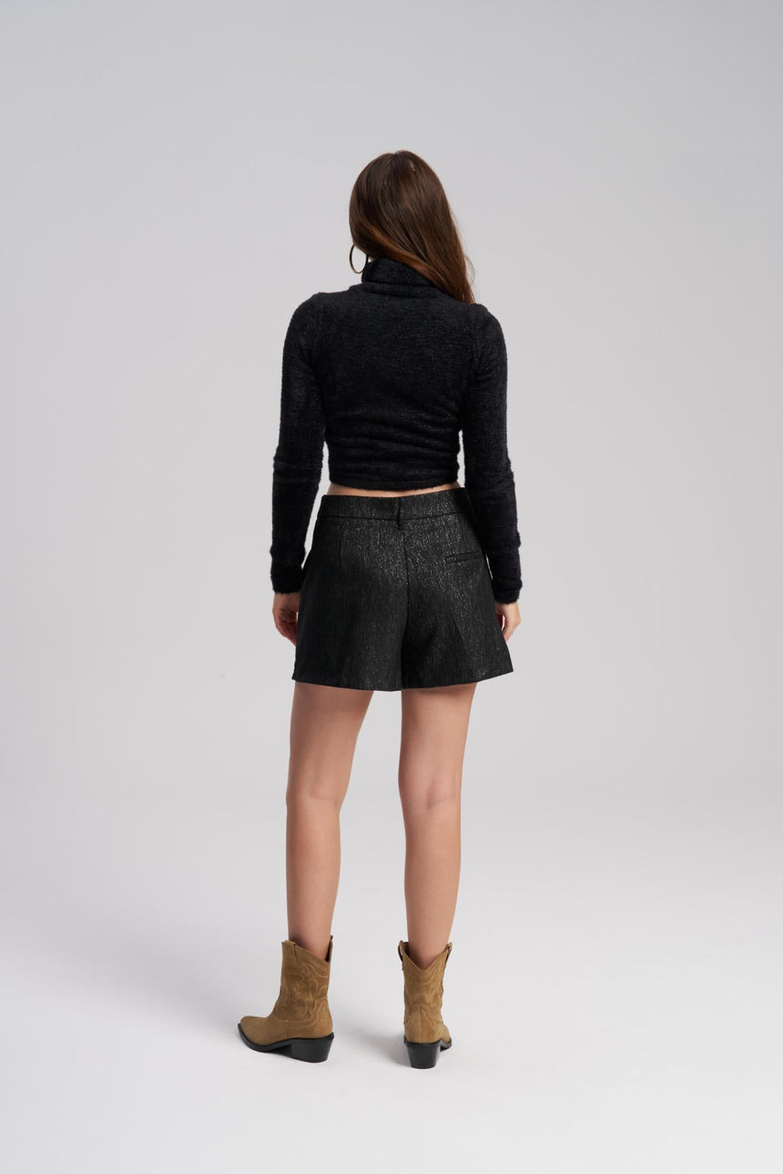 Person wearing a black turtleneck, gray shorts, and brown boots on a white background