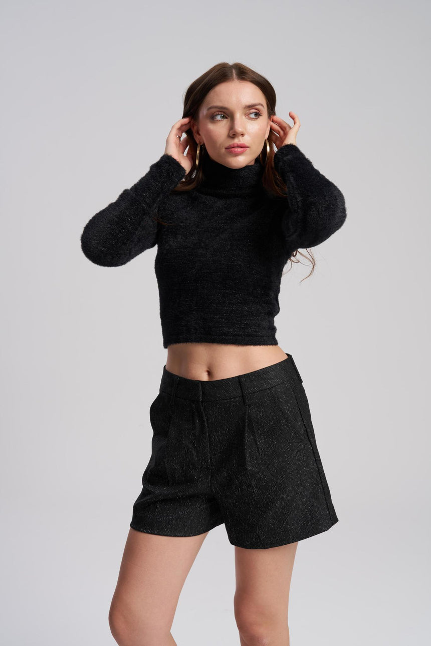 Woman wearing a black turtleneck sweater and black shorts on a gray background