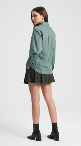 Woman wearing a green patterned shirt and black pleated skirt on a white background