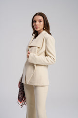 Woman wearing a beige suit with a patterned scarf on a gray background side viw