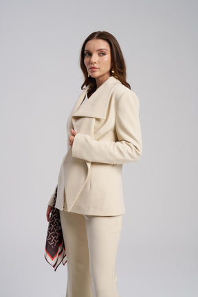 Woman wearing a beige suit with a patterned scarf on a gray background side viw