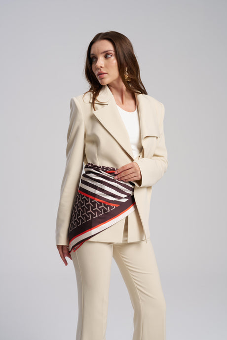 Woman wearing a beige suit with a patterned scarf on a gray background