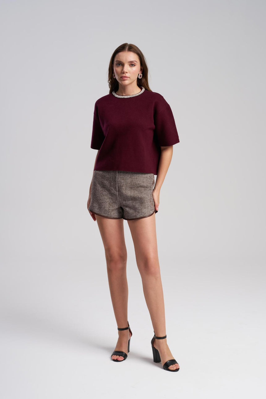 Woman wearing a burgundy top and patterned shorts on a white background