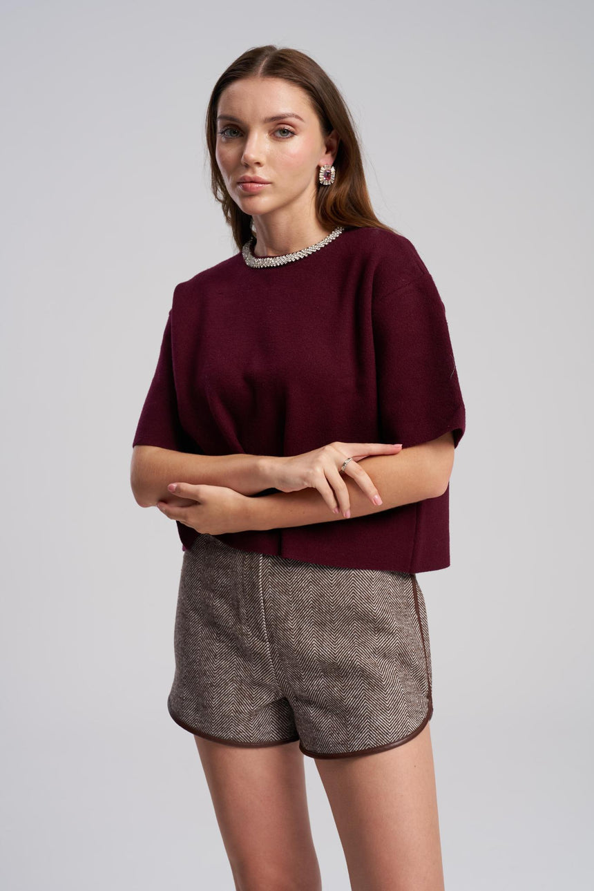 Woman wearing a burgundy top and gray shorts on a plain background