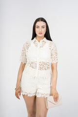 A woman modeling a white lace short-sleeve collared top and matching lace shorts, 