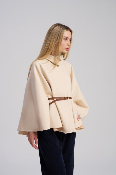 Woman wearing a beige cape with a brown belt on a gray background