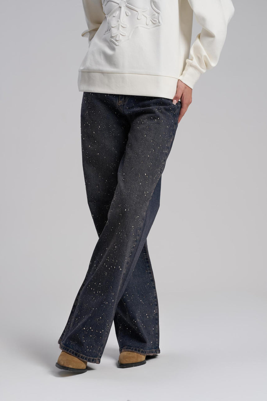 Person wearing dark blue flared jeans and a light-colored hoodie on a plain background