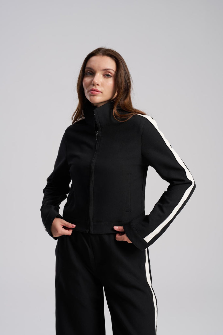 Woman wearing a black tracksuit with white stripes on a gray background