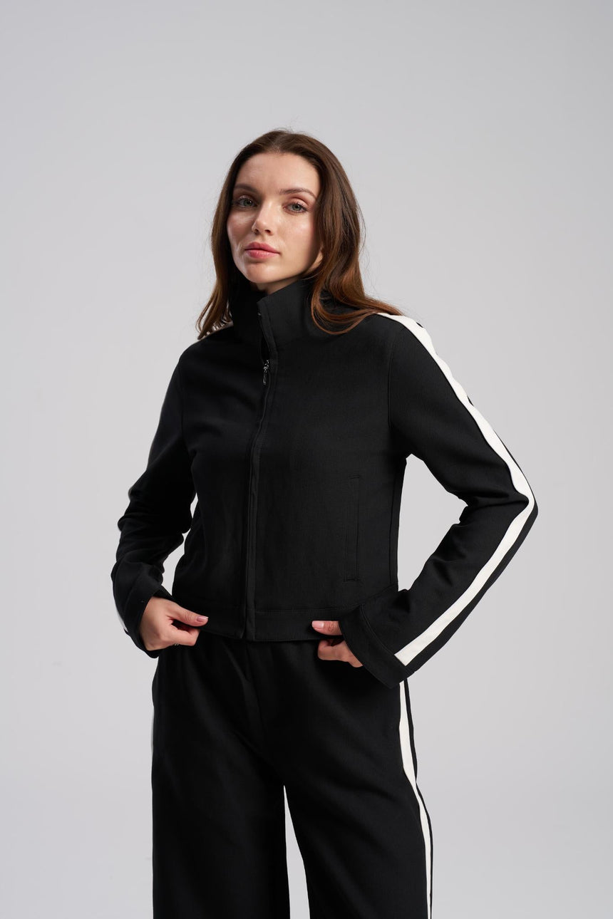 Woman wearing a black tracksuit with white stripes on a gray background