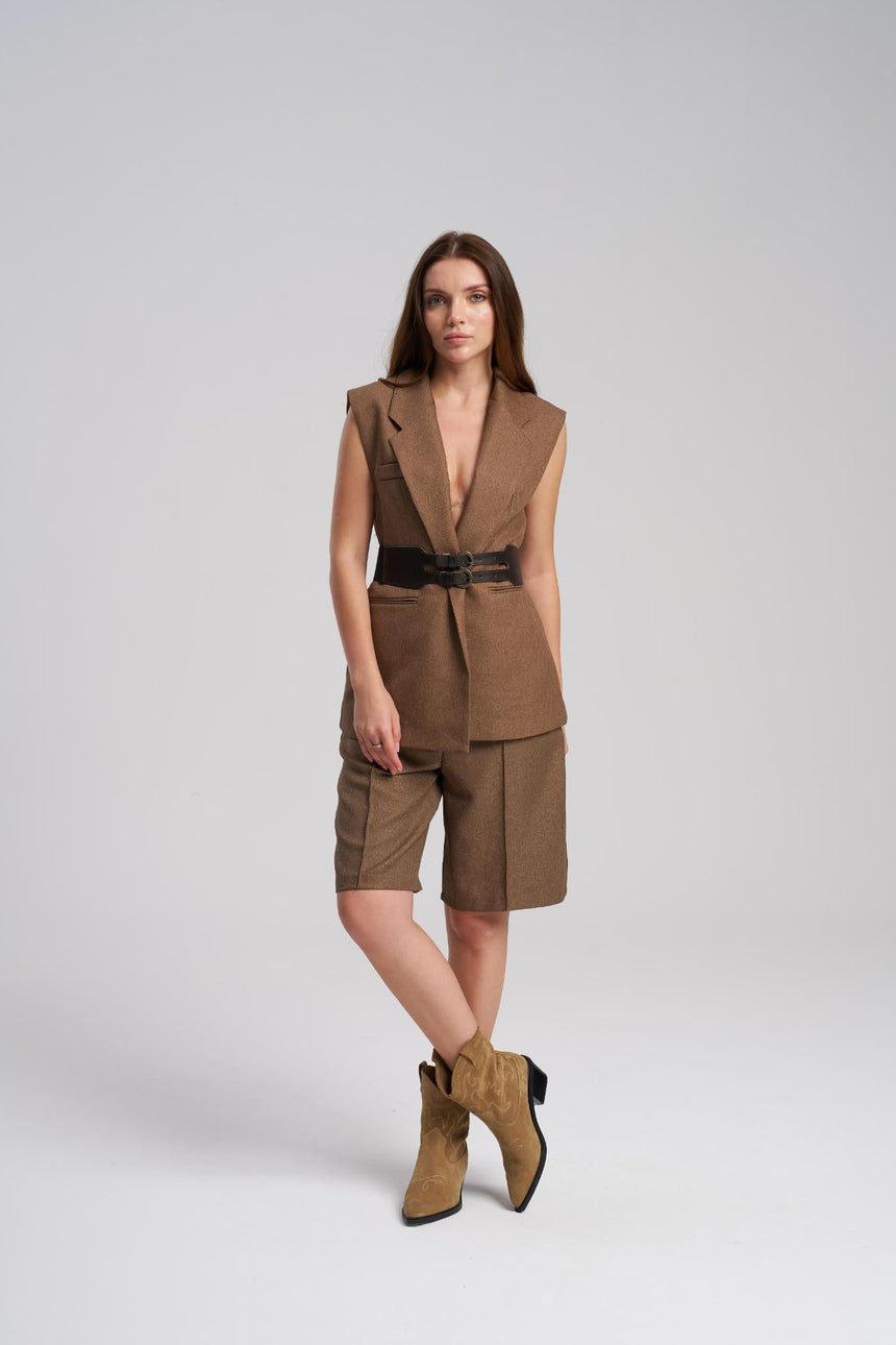 Woman wearing a brown sleeveless blazer, shorts, and boots on a white background