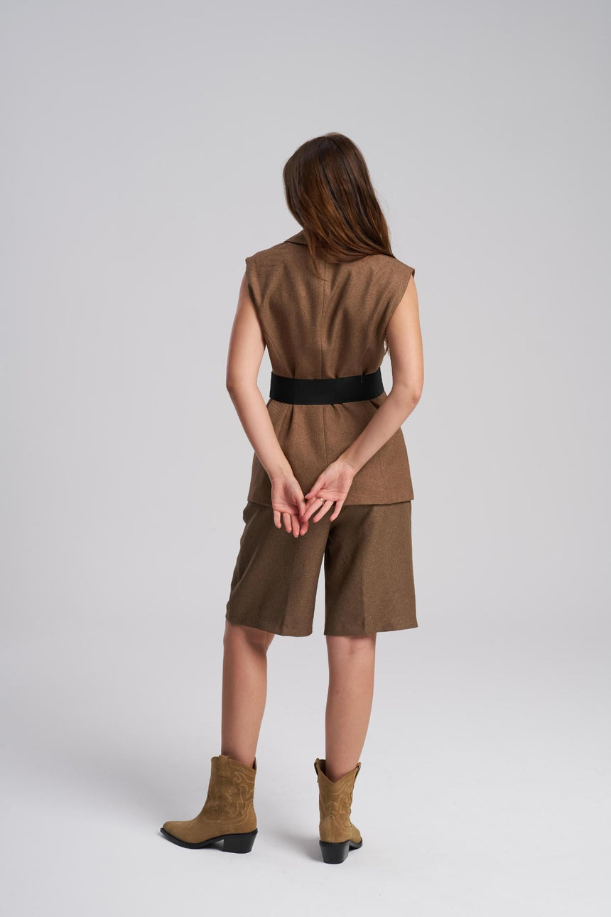 Person wearing a brown sleeveless top and shorts with a belt, standing against a white background