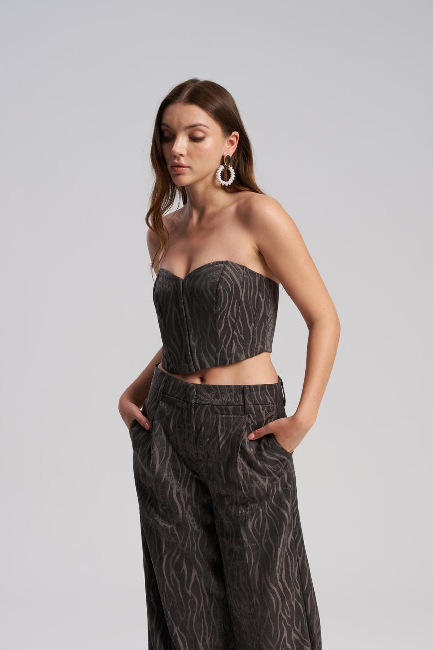 Woman wearing a dark patterned strapless top and high-waisted pants on a light gray background