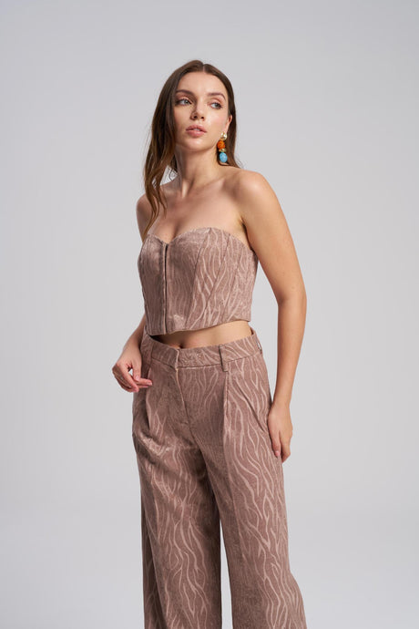 Woman wearing a patterned strapless top and pants on a plain background