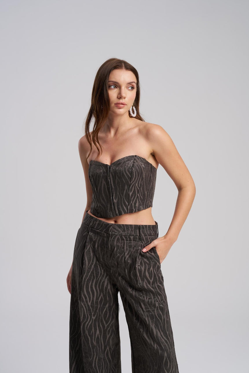 Woman wearing a strapless top and wide-leg pants with a textured pattern on a gray background