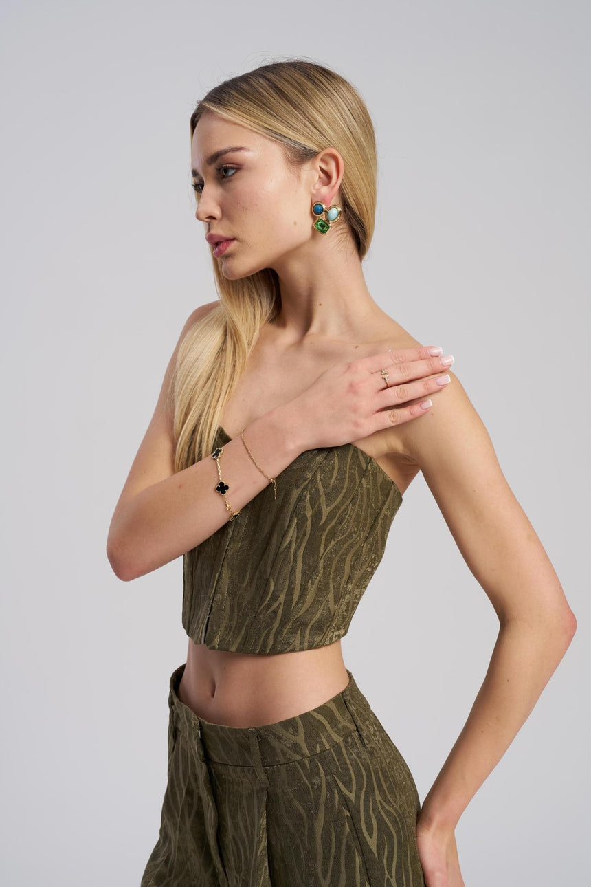Woman wearing a green patterned outfit with jewelry on a plain background