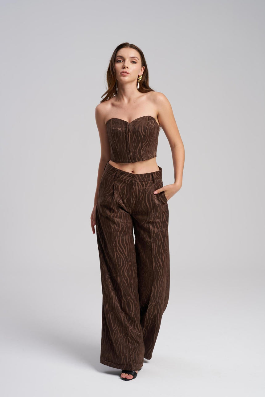 Woman wearing a brown strapless top and wide-leg pants on a light gray background
