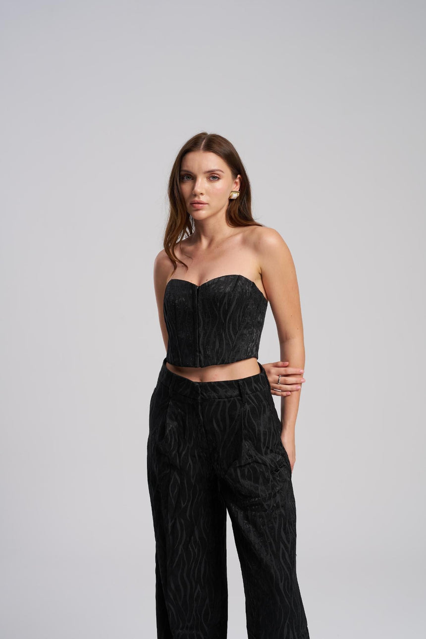 Woman wearing a black strapless top and high-waisted pants on a gray background