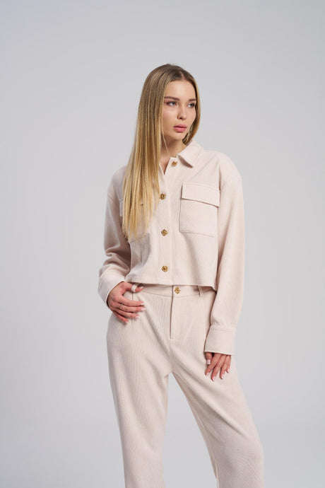 Woman wearing a beige outfit with a jacket and pants on a plain background
