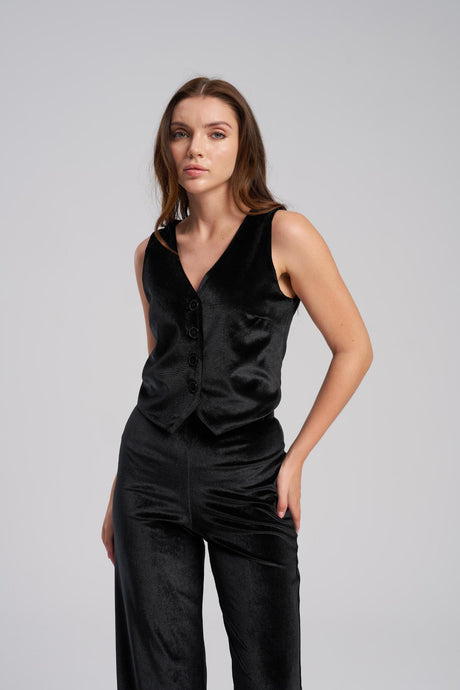 Woman wearing a black sleeveless vest and pants against a gray background