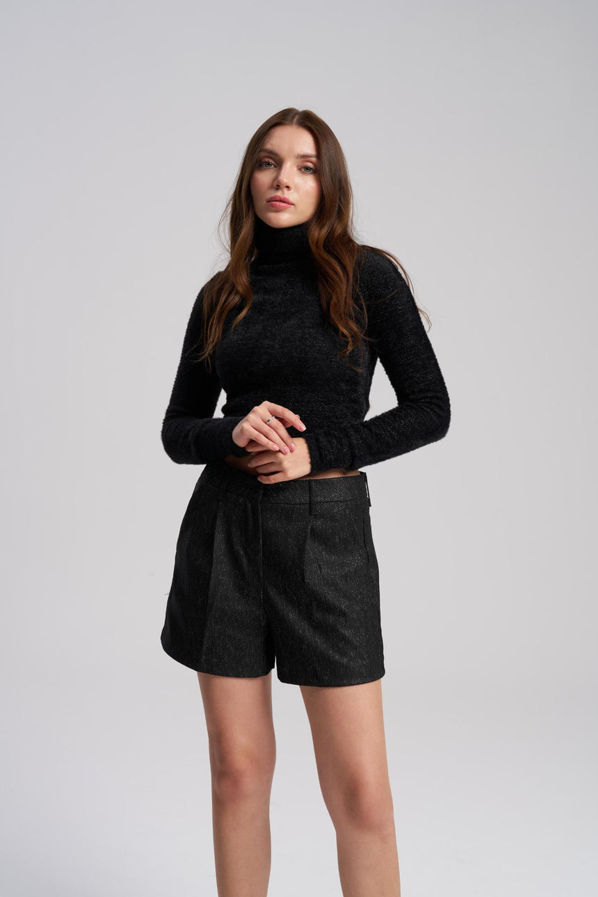 Woman wearing a black turtleneck and black shorts on a light gray background
